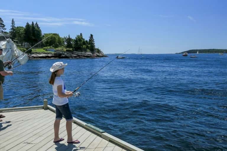 Young girl fishing from wooden dock overlooking calm blue water and forested shoreline