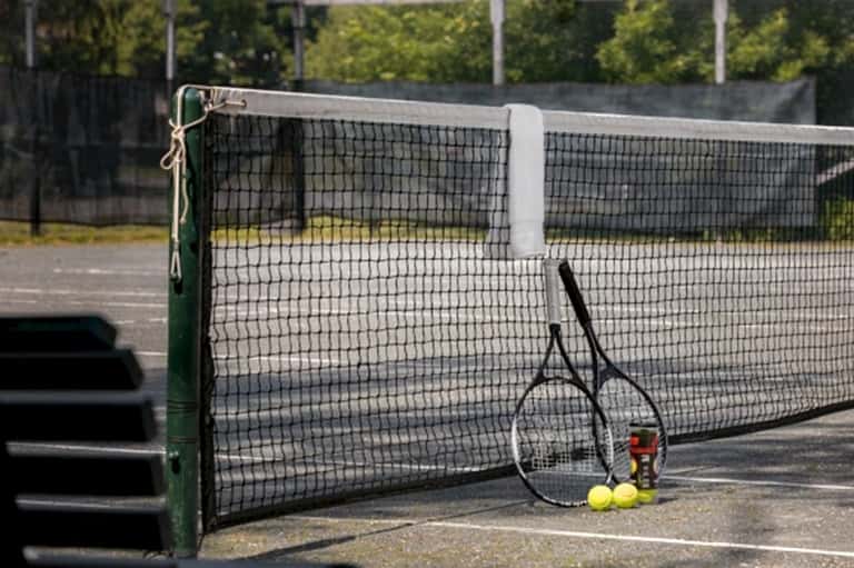 Professional tennis court with net, racket, yellow balls, and sports equipment on concrete surface