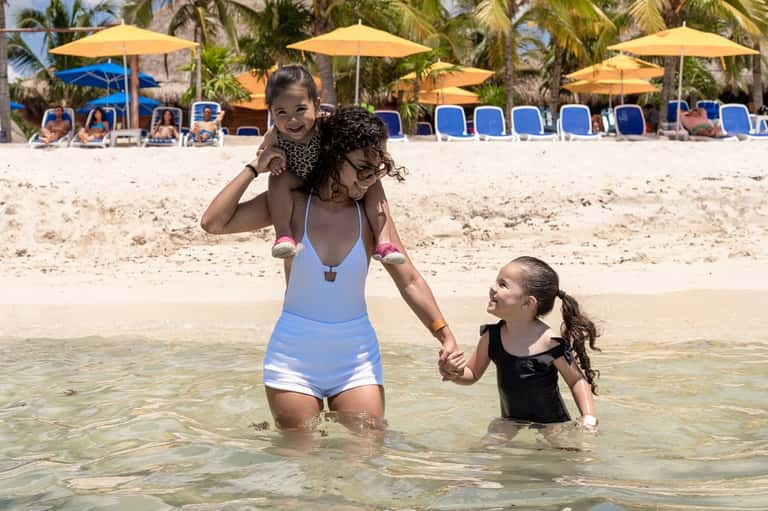 Woman in swimsuit with children wading in clear tropical ocean waters at beach