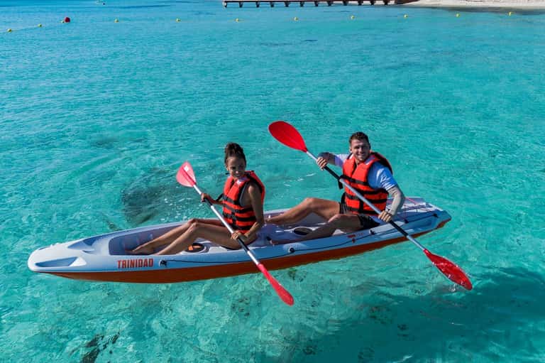 Two people kayaking in crystal clear turquoise water near coastal resort