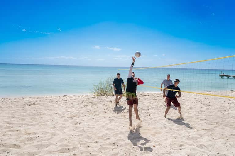 Beach volleyball game with players jumping to hit ball over net under clear blue sky