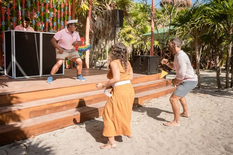 Guests playing cornhole on a beach with palm trees, performance stage, and colorful decorations