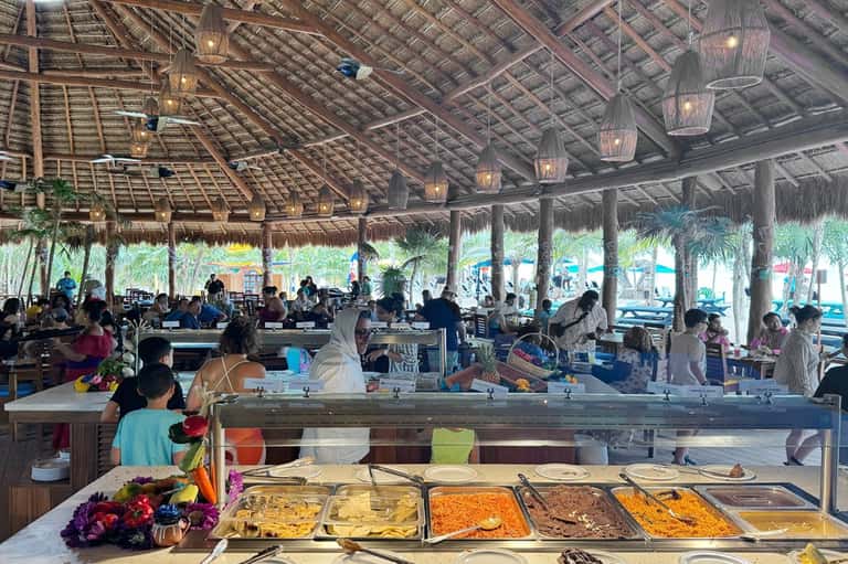 Beach resort buffet dining area with thatched roof, food stations, and ocean view beyond