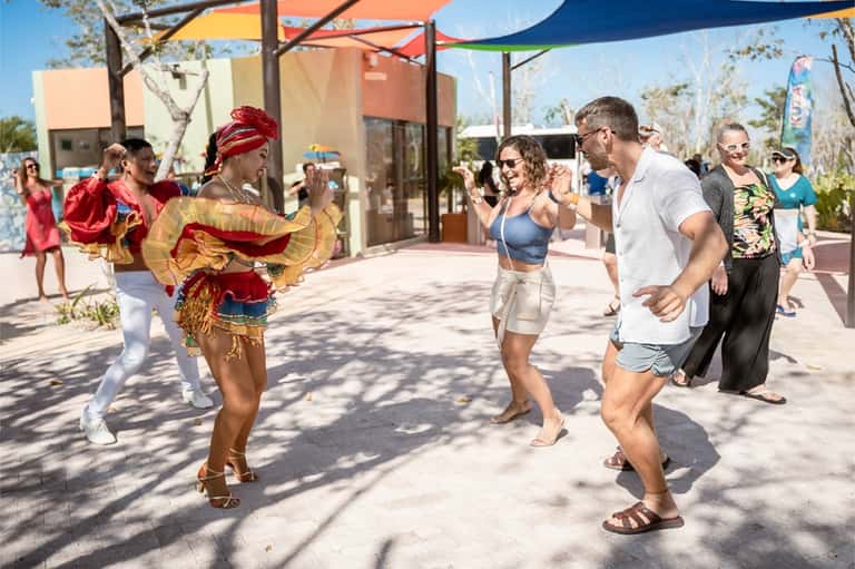 Guests dancing with entertainers under colorful shade sails at beachfront resort