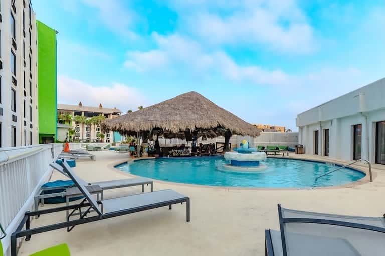 Resort pool with thatched roof cabana, lounge chairs, and palm tree landscaping