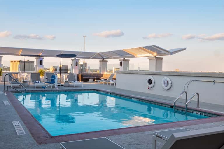 Rooftop pool with blue water, modern pergola shade structure, and city skyline views