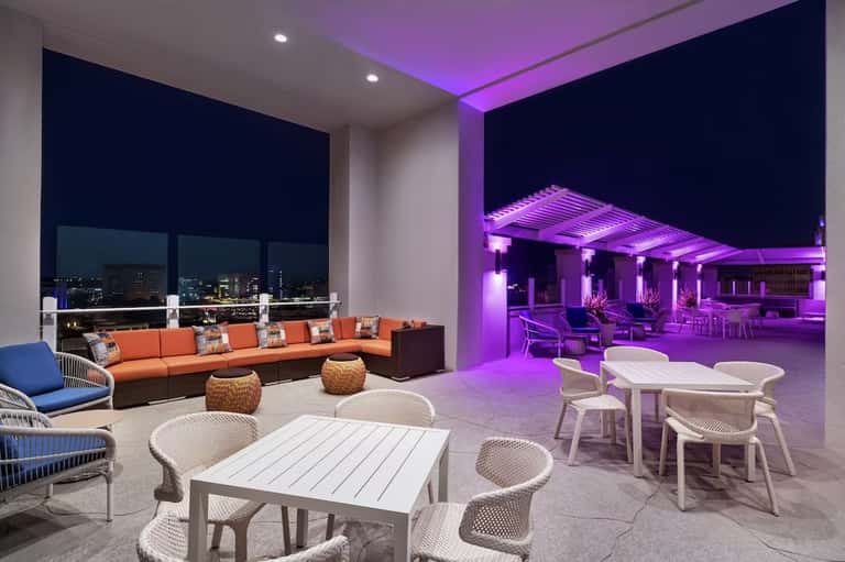 Modern resort terrace with purple ambient lighting, orange seating, and city skyline views