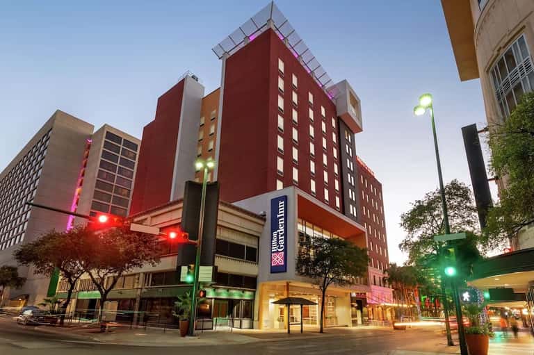 Modern red and tan hotel building at dusk with street-level entrance and urban setting