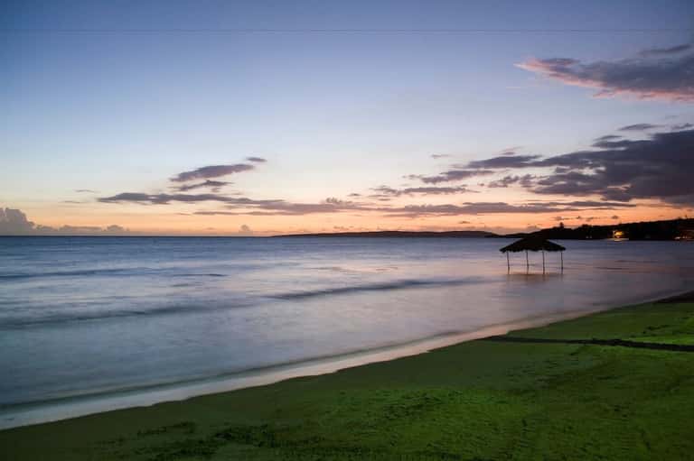 Serene sunset beach with calm ocean waters, sandy shore, and covered cabana at twilight