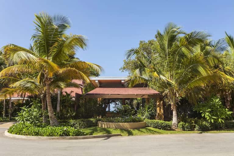 Tropical resort entrance with palm trees, tan metal pergola, and landscaped grounds