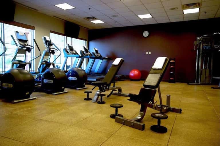 Fitness center with cardio equipment including stationary bikes, exercise machines, free weights, and red accent wall