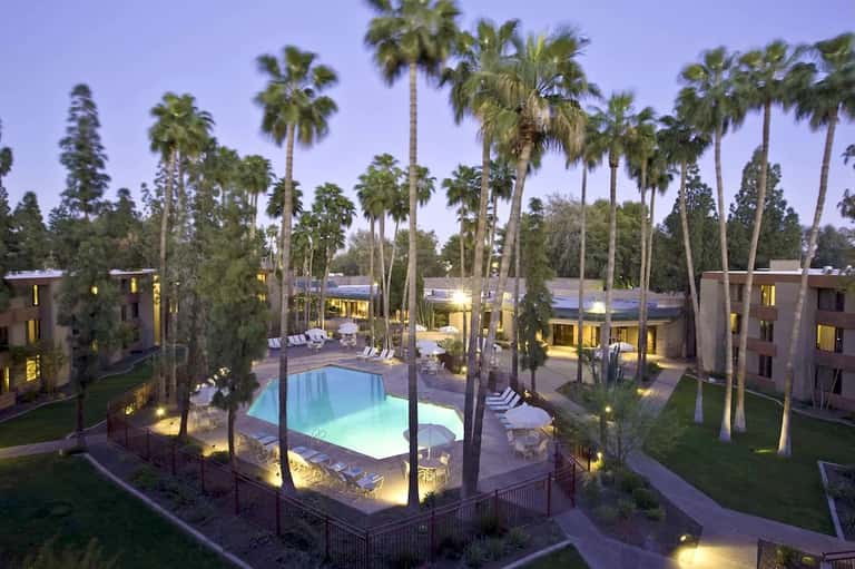 Resort courtyard at dusk featuring illuminated pool surrounded by palm trees and multi-story buildings