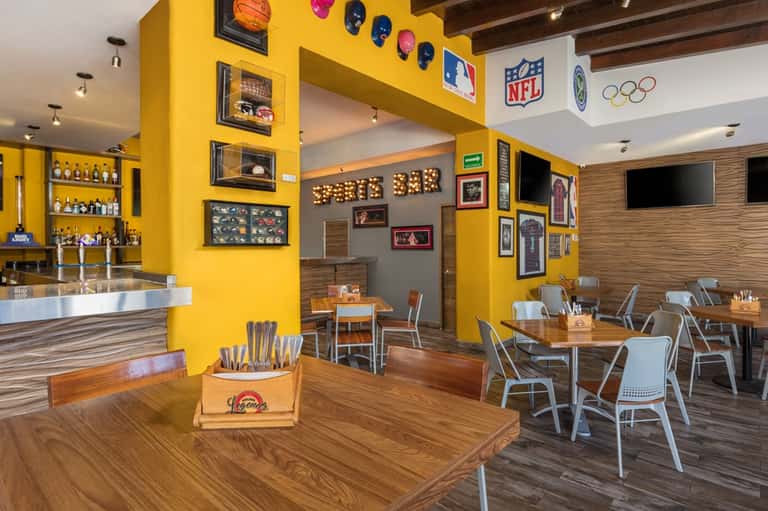 Sports bar interior with bright yellow accent walls, wood flooring, bar counter, and TV screens