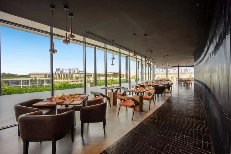 Modern dining area with floor-to-ceiling windows, wooden tables, and brown leather chairs overlooking landscape
