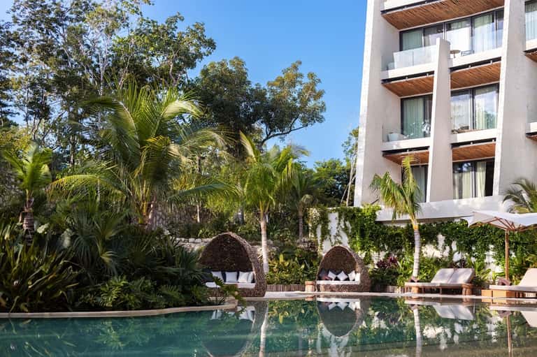 Luxury resort pool with palm trees, woven lounge chairs, umbrellas, and modern building with wooden accents