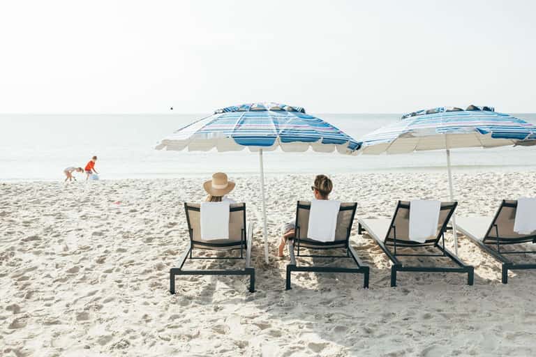 Beach lounge area with striped umbrellas, loungers, and ocean view with children playing