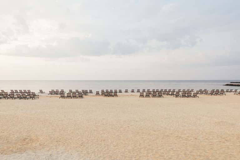 Beach scene with rows of empty lounge chairs lined along sandy shore and calm ocean