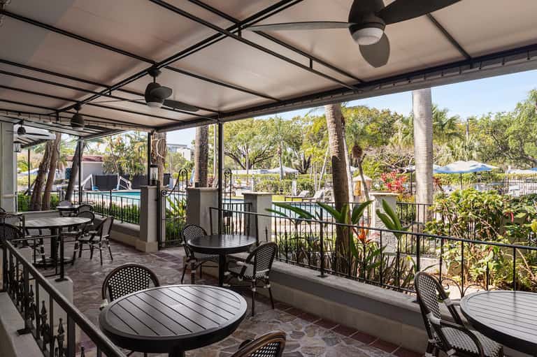 Covered outdoor dining area with tables and chairs overlooking resort grounds and pool