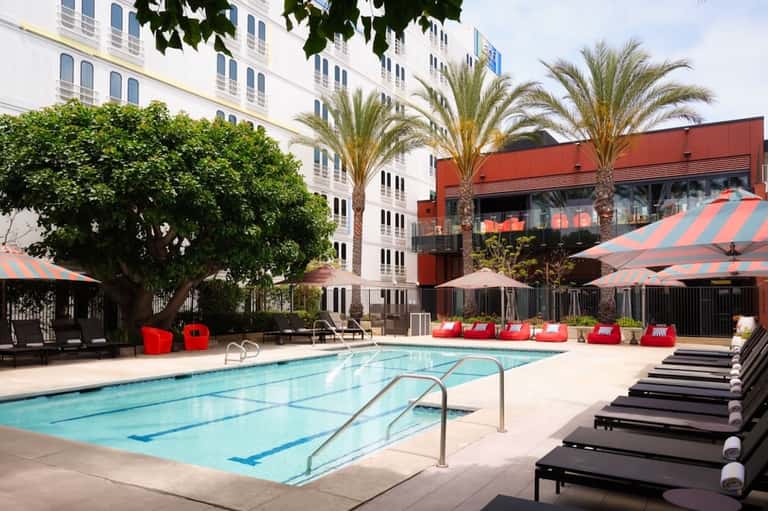 Modern hotel pool with lap lanes, red umbrellas, loungers, and contemporary red-accented building facade