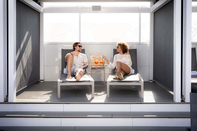 Two guests relaxing on a modern rooftop terrace with white lounge chairs and city views