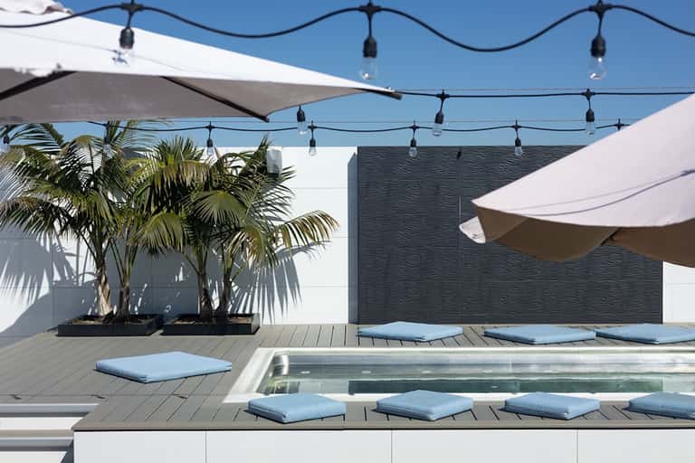 Contemporary rooftop pool deck with loungers, shade sails, and string lighting