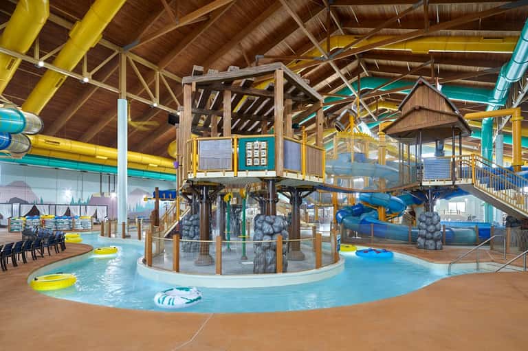 Indoor water park with wooden treehouse structure, water slides, and shallow pool for children