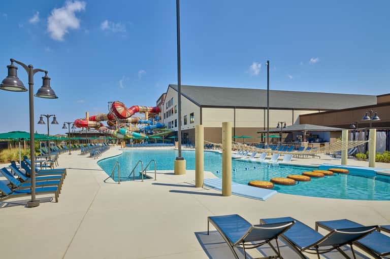 Daytime resort pool with waterslide, multiple pools, and blue lounge chairs