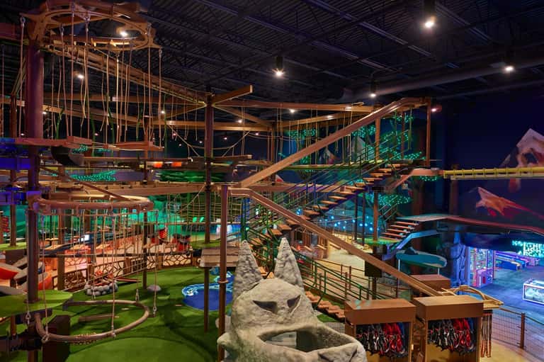 Indoor adventure park with multi-level wooden structures, rope courses, and climbing obstacles