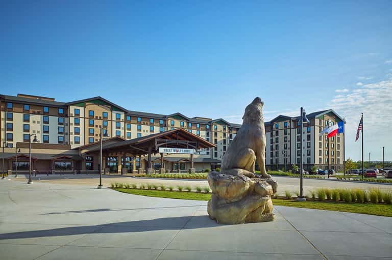 Great Wolf Lodge exterior with tall bear statue, building entrance, flags, and manicured grounds on sunny day