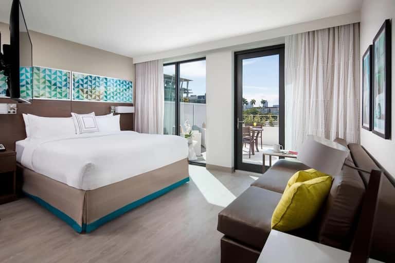 Modern hotel bedroom with king bed, balcony access, ocean view, and contemporary furnishings