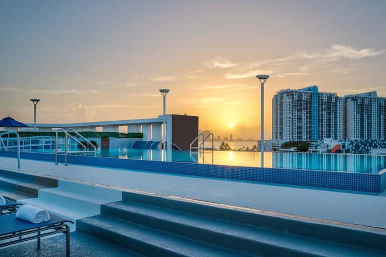 Rooftop infinity pool at sunset with city skyline and high-rise buildings reflected in calm water