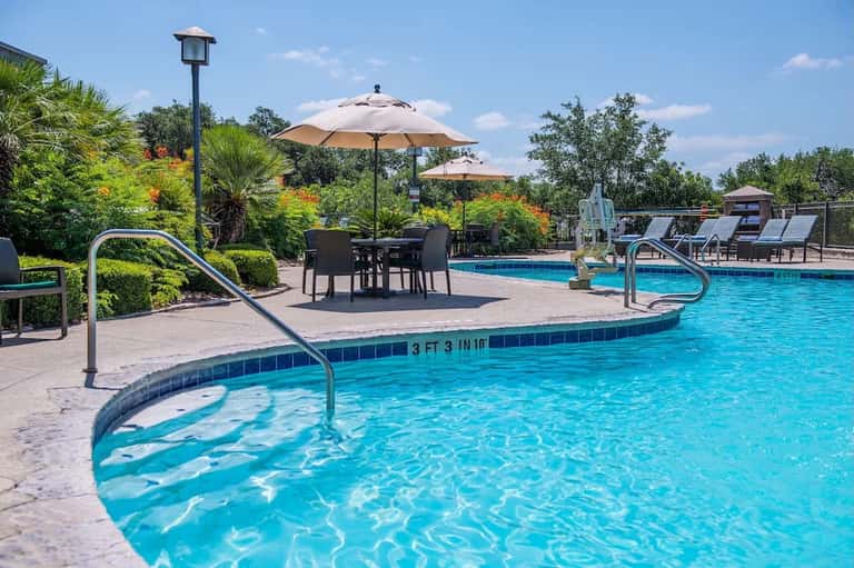 Resort pool with curved spa, umbrellas, dining tables, and lush landscaping