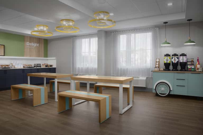 Modern cafeteria with wooden tables, white benches, turquoise accents, pendant lights, and large bright windows