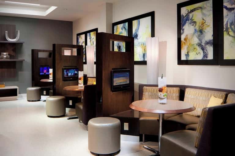 Contemporary hotel lobby lounge with dark wood room dividers, cream seating, and abstract framed artwork