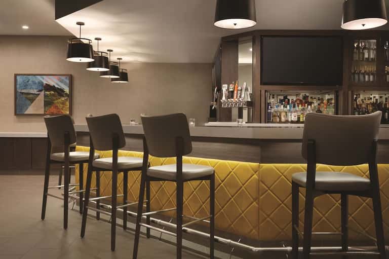 Contemporary lounge bar with yellow quilted seating, black chairs, pendant lights, and full bar