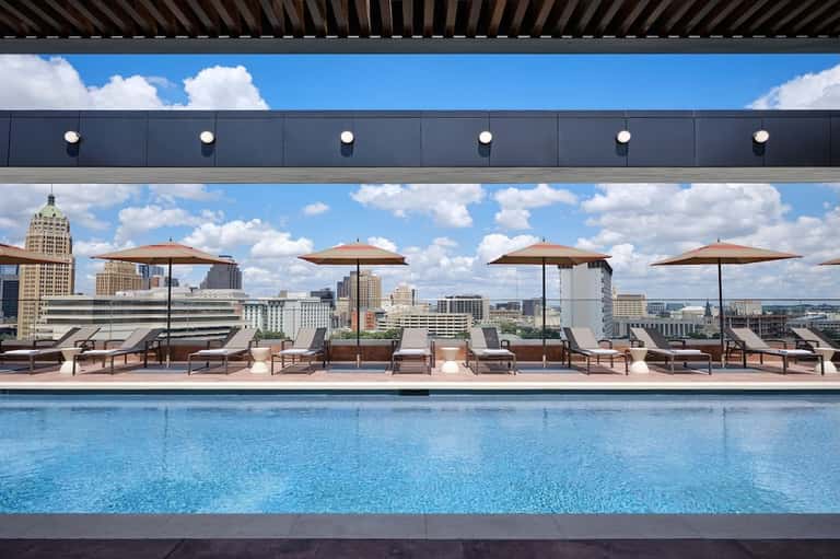 Modern rooftop infinity pool with lounge seating, umbrellas, and panoramic city skyline views at daytime