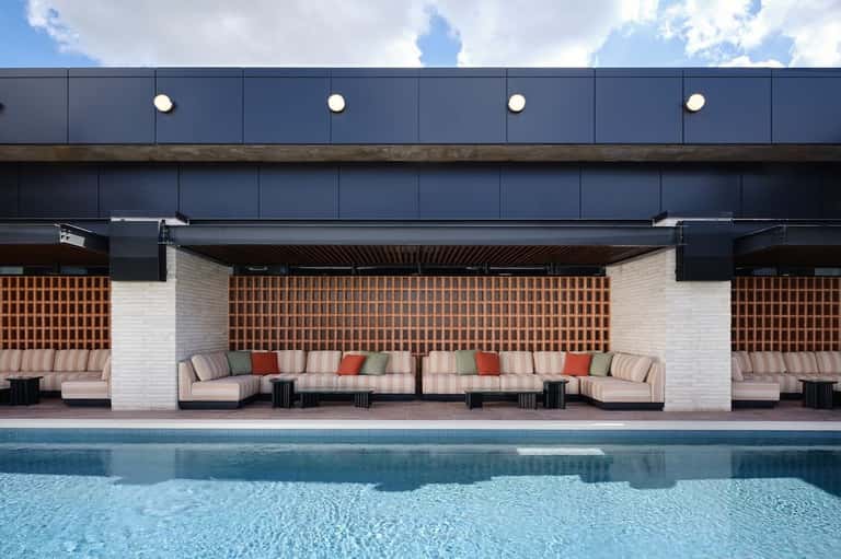 Modern poolside cabana with brick accent wall, striped lounge seating, and blue water reflection