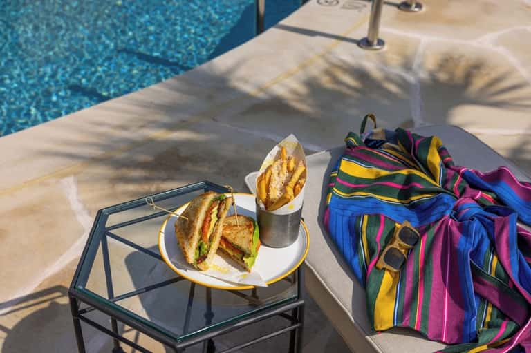 Poolside lunch with sandwich, drink, and colorful striped beach towel