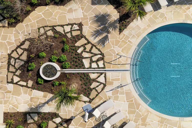 Outdoor pool with decorative paving, palm trees, and overhead view of poolside landscape