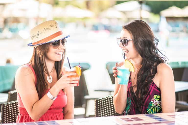 Two women enjoying colorful tropical drinks by the poolside at a resort
