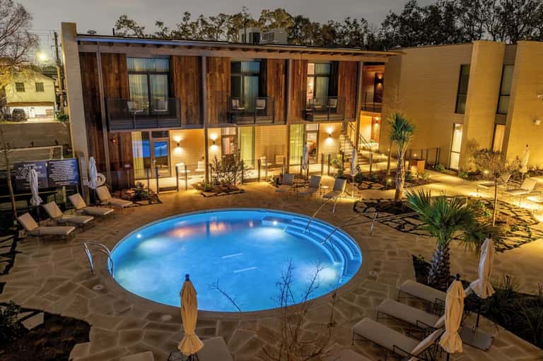 Illuminated modern residential courtyard with circular lit pool, wooden building with large windows, evening setting