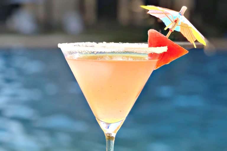Tropical cocktail with salt rim, pineapple garnish, and umbrella against ocean backdrop