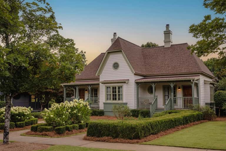 Charming cottage-style house with white siding, brown roof, and manicured landscaping
