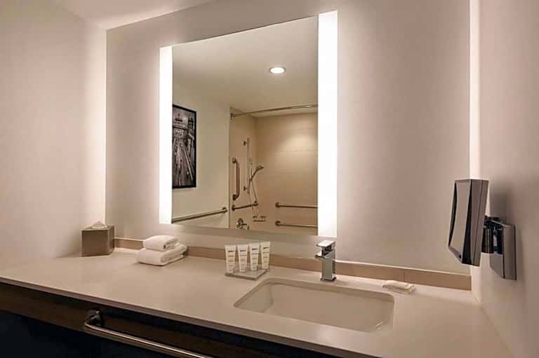 Luxury bathroom vanity with large illuminated mirror, white countertop, sink, and toiletries displayed