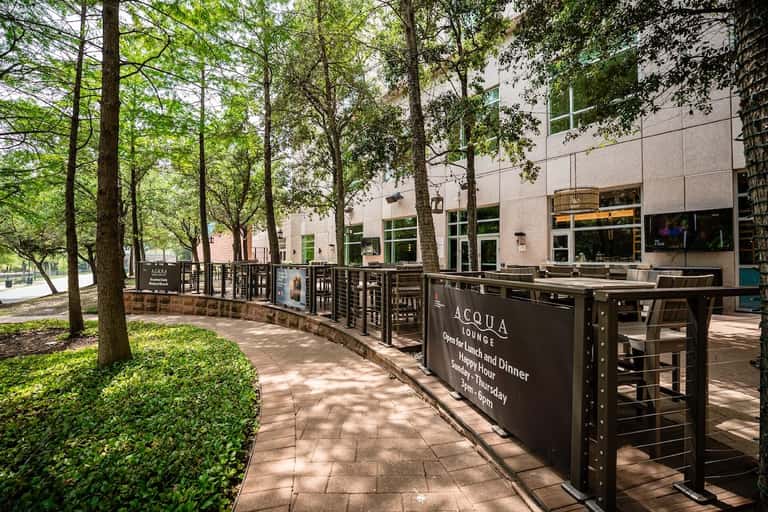 Outdoor restaurant patio with wooden fence, brick pavers, and modern building facade