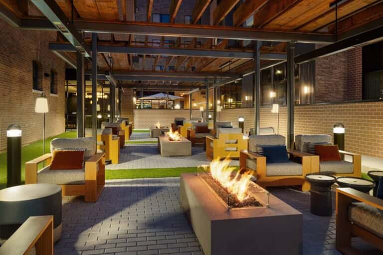 Modern covered outdoor patio with fireplace, lounge seating, exposed wooden beams, and ambient lighting