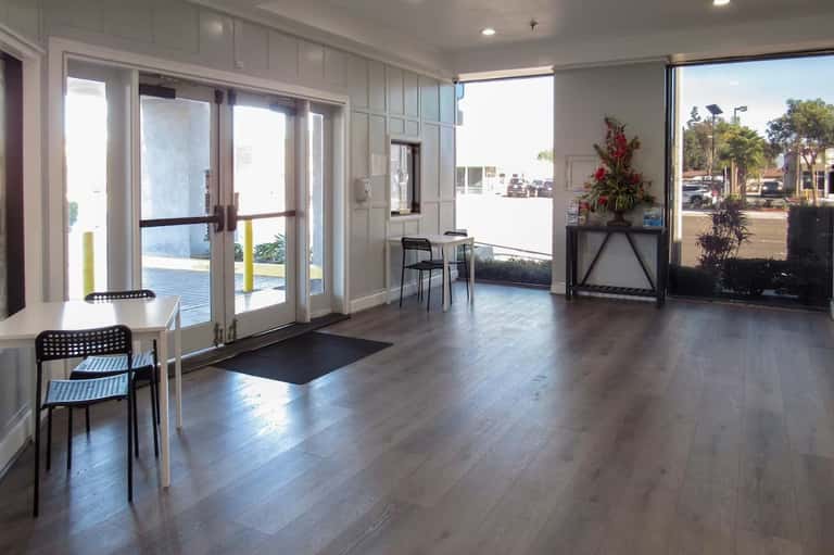 Bright hotel lobby with glass doors, wood flooring, and ocean view access