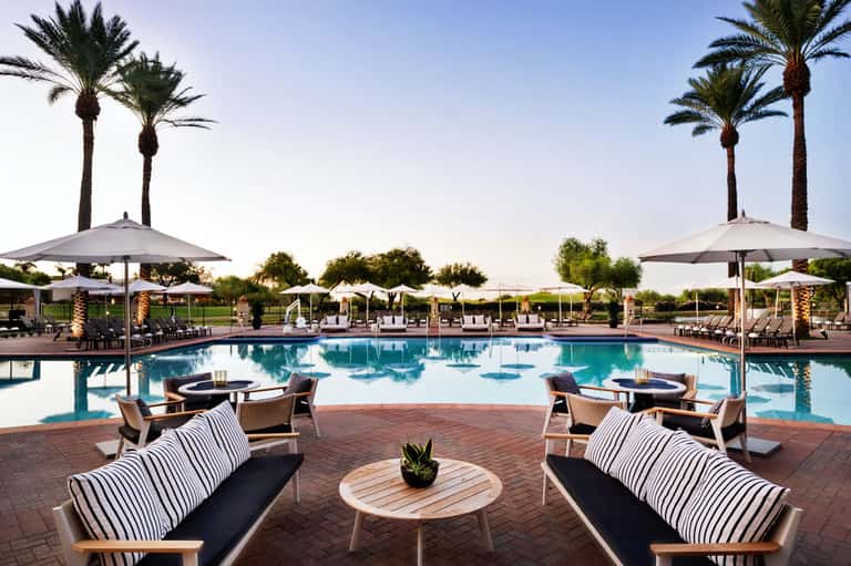 Luxurious resort pool surrounded by palm trees, lounge chairs, and large umbrellas at dusk