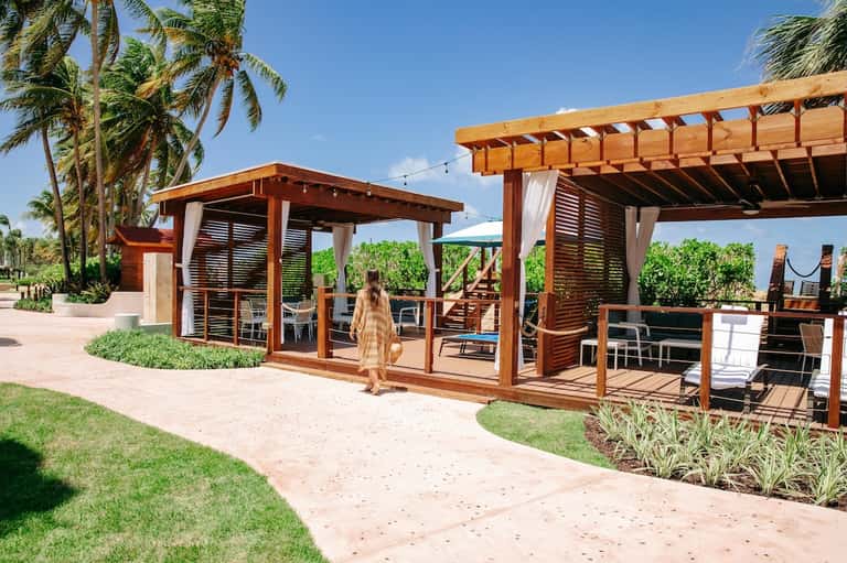 Wooden pergola structures with string lights on beachfront resort grounds surrounded by palm trees