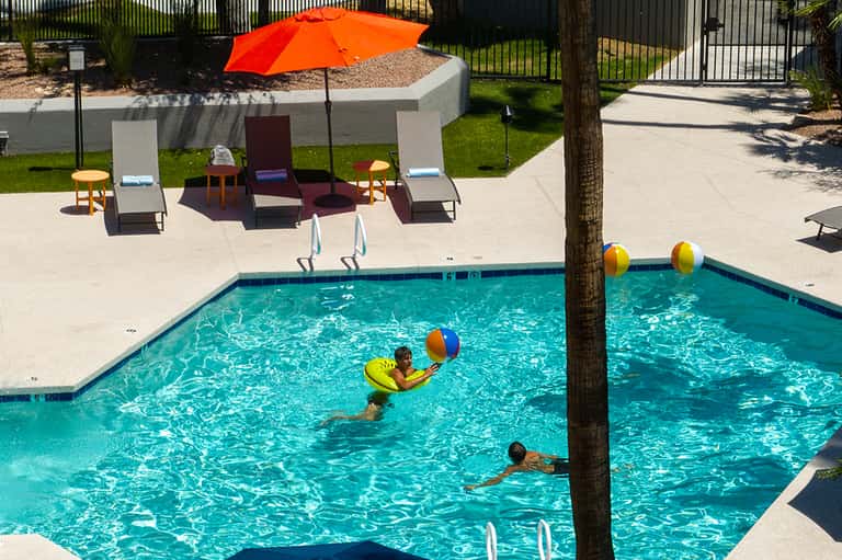 Children playing in bright turquoise resort pool with colorful umbrellas and beach loungers
